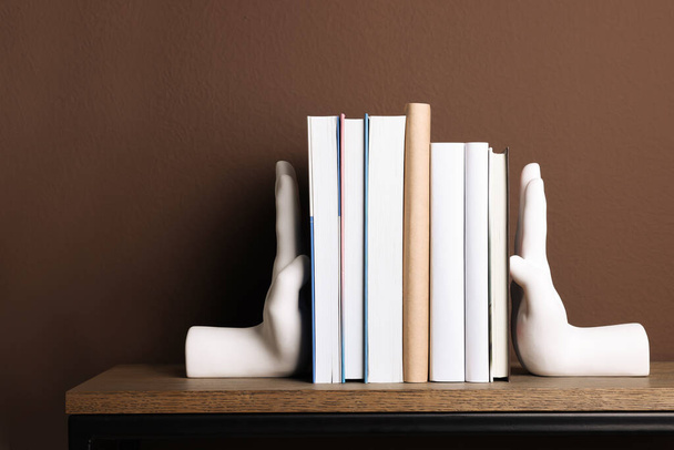 Güzel el şekilli kitap destekleri ve kahverengi duvarın yanındaki raflarda kitaplar. - Fotoğraf, Görsel