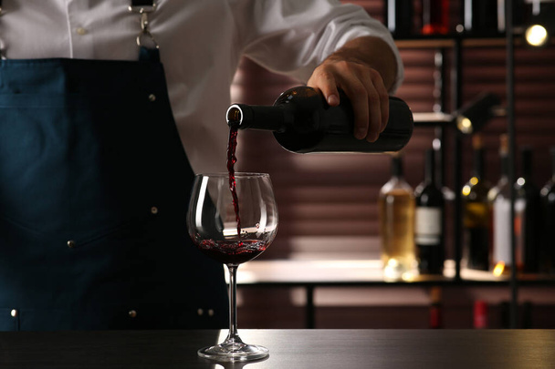 Bartender pouring red wine into glass at counter indoors, closeup - Фото, зображення