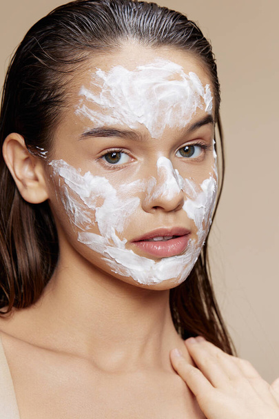 Brünette Anwendung einer beruhigenden Gesichtsmaske Hautpflege beige Hintergrund - Foto, Bild