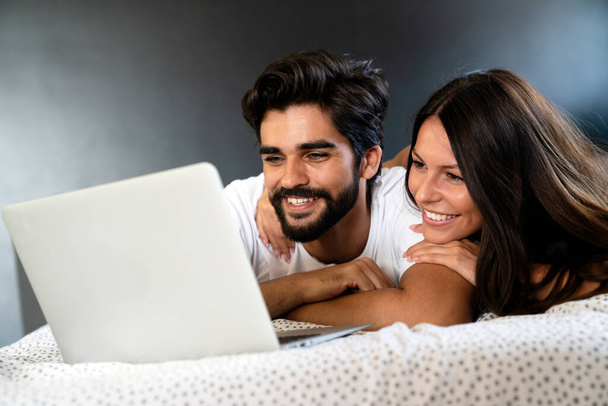 Happy couple with laptop in bed reading news and smiling - 写真・画像