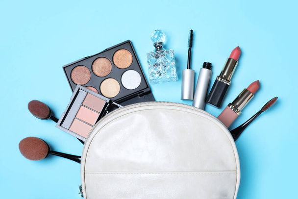 Cosmetic bag and makeup products with accessories on light blue background, flat lay - 写真・画像