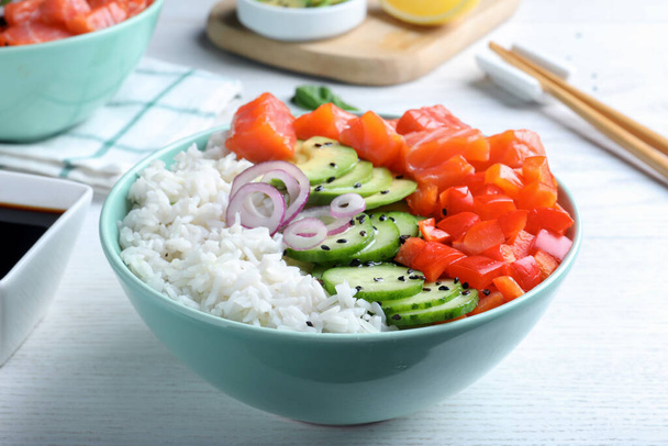 Delicious poke bowl with salmon and vegetables served on white wooden table,closeup - Fotó, kép