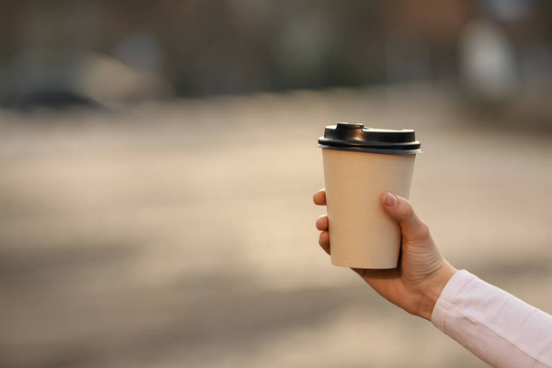 Woman holding paper coffee cup outdoors, closeup. Space for text - Photo, Image