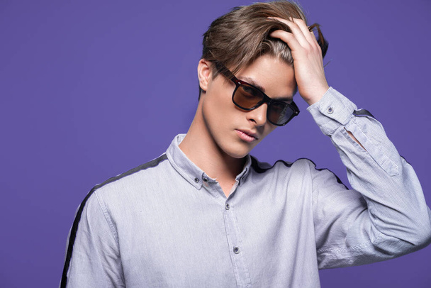 Male hairstyle concept. Hipster guy with stylish haircut in sunglasses stands over lilac background. - 写真・画像
