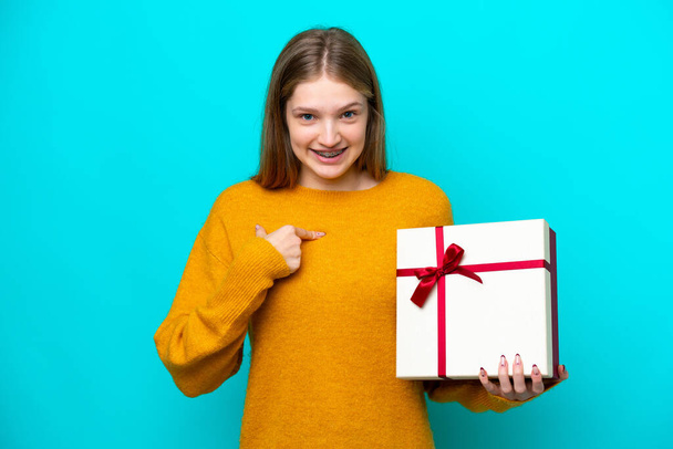 Teenager Russian girl holding a gift isolated on blue background with surprise facial expression - Fotó, kép