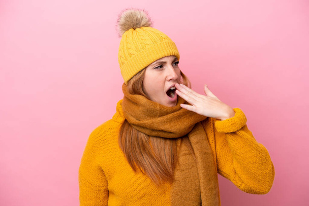 Young redhead woman wearing winter jacket isolated on pink background yawning and covering wide open mouth with hand - Foto, imagen