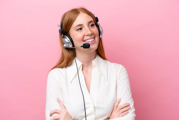 Telemarketer vörös hajú nő dolgozik egy headset elszigetelt rózsaszín háttér boldog és mosolygós - Fotó, kép