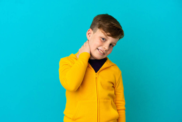 Ένα μικρό κοκκινομάλλικο αγόρι απομονωμένο σε μπλε φόντο γελώντας - Φωτογραφία, εικόνα