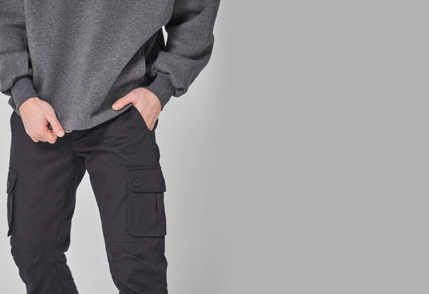 Schnappschuss eines Mannes in dunkelgrauem Sweatshirt und schwarzer Hose. Steht auf grauem Hintergrund. Mockup für Druck oder Design-Vorlage. Grundlegende Bekleidungslinie ohne Logo - Foto, Bild