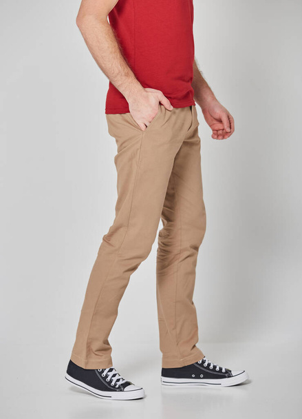 Schnappschuss eines Mannes in rotem T-Shirt und beiger Hose. Steht auf grauem Hintergrund. Mockup für Druck oder Design-Vorlage. Grundlegende Bekleidungslinie ohne Logo - Foto, Bild