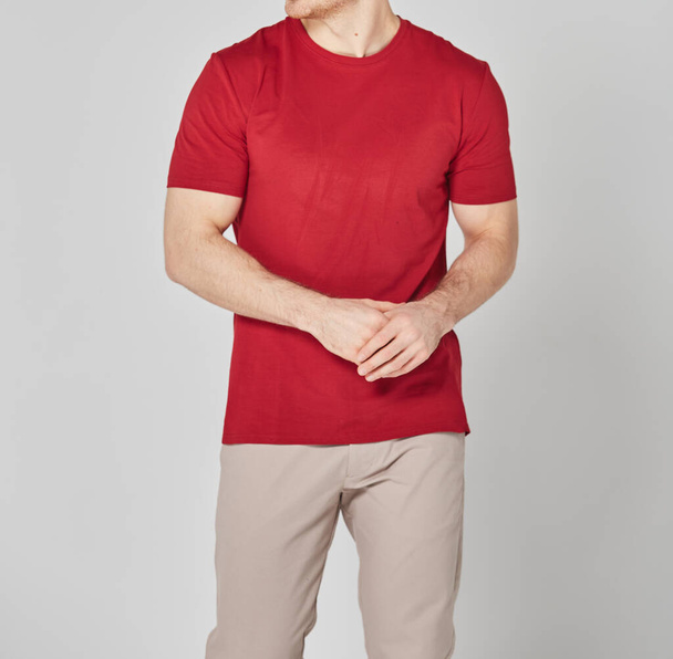 Gehakt van de man in rood wit t-shirt en beige broek. Staande op grijze achtergrond. Mockup voor print of design sjabloon. Basic kledinglijn geen logo - Foto, afbeelding