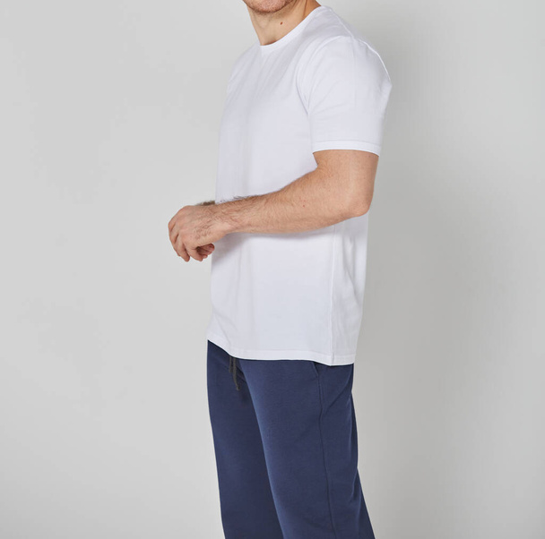 Schnappschuss eines Mannes in weißem T-Shirt und blauer Hose. Steht auf grauem Hintergrund. Mockup für Druck oder Design-Vorlage. Grundlegende Bekleidungslinie ohne Logo - Foto, Bild