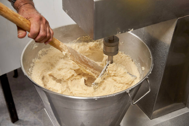 Close-up of a cooks hands stirring raw dough with a stick to make churros.  - Foto, imagen