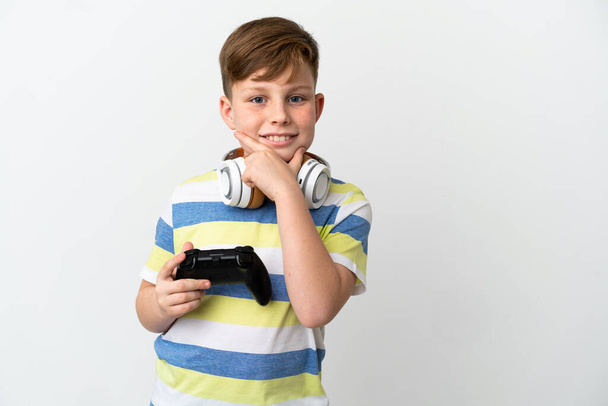 Mały rudy chłopiec trzyma gra pad odizolowany na białym tle szczęśliwy i uśmiechnięty - Zdjęcie, obraz