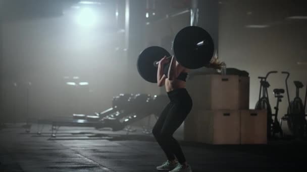 Женщина бодибилдер делает упражнения с гирями в спортзале. Женщина-тяжелоатлетка делает штангу в тёмном спортзале. Женщина-культурист делает упражнения по поднятию веса на тренировке хардкор - Кадры, видео