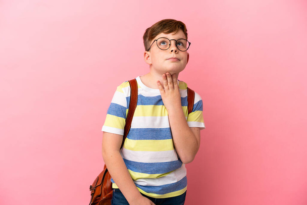 Little redhead caucasian boy isolated on pink background looking up while smiling - 写真・画像