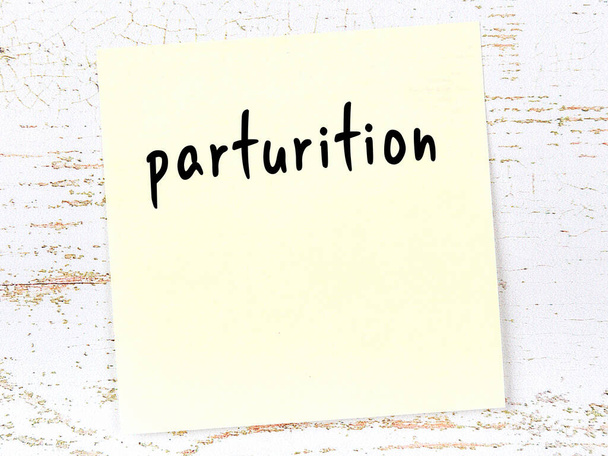 Concept of reminder about parturition. Yellow sticky sheet of paper on wooden wall with inscription - Photo, Image