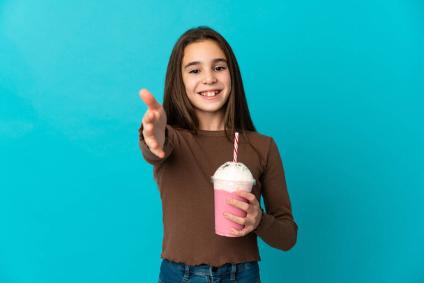 Mała dziewczynka z truskawkowym shake 'iem odizolowana na niebieskim tle ściskając dłonie za zamknięcie dobrej umowy - Zdjęcie, obraz