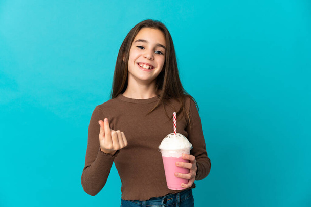 Kislány eper tejturmix elszigetelt kék háttér, hogy pénzt gesztus - Fotó, kép