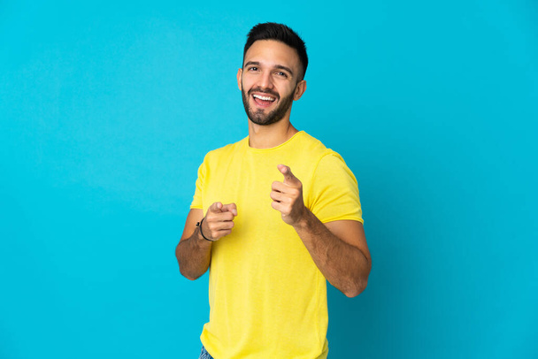 Young caucasian man isolated on blue background surprised and pointing front - Foto, Imagen
