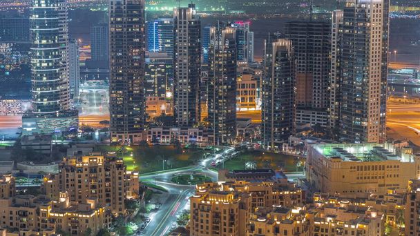 Aerial view of traffic on circle intersection a big futuristic city night timelapse. Business bay and Downtown district with many skyscrapers and traditional houses, Dubai, United Arab Emirates skyline. - Φωτογραφία, εικόνα