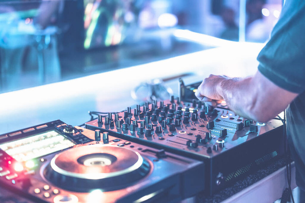 DJ, gece kulübündeki tekno partisinde parlak mavi sahne ışıklarıyla müzik çalıyor. Konserde müzik parçalarını karıştıran profesyonel disk jokeyi. Dj el ses düzeyi düğmesini ayarlıyor. - Fotoğraf, Görsel