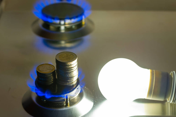 Vedle zapáleného plynového sporáku se rozsvítí žárovka a vedle ní mince. Náklady na energii a plyn, zvýšení nákladů. - Fotografie, Obrázek