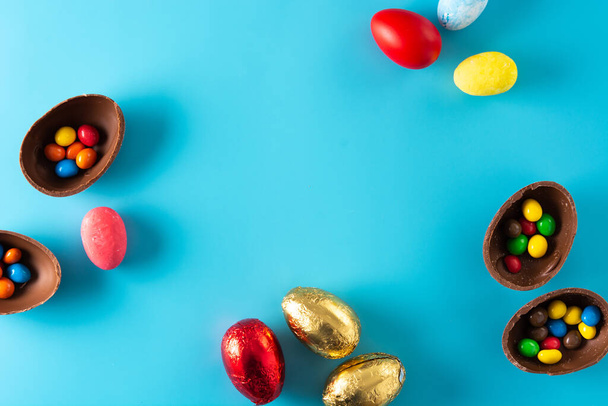 Colorful chocolate Easter eggs on blue bckground. Top view. Copy space - 写真・画像