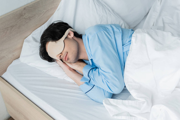 young man in sleep mask and pajamas sleeping on white bedding - Foto, immagini