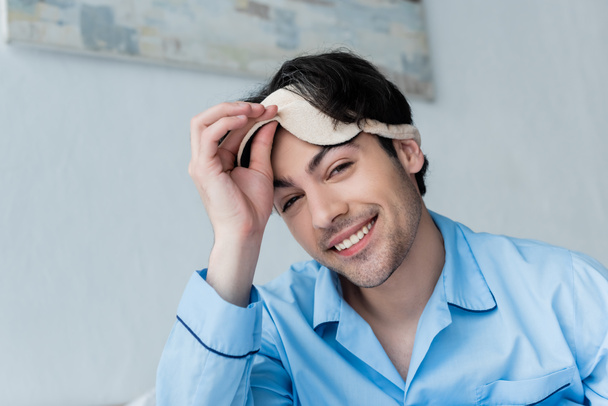 cheerful young man taking off sleep mask and looking at camera - Photo, Image