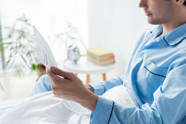 cropped view of man in blue pajamas reading morning newspaper in bed - Photo, image