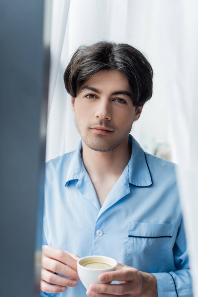 young brunette man in blue pajamas looking at camera on blurred foreground - Foto, Imagem