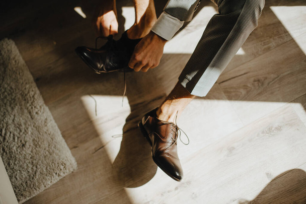 Ένας άντρας με κοστούμι, ο γαμπρός, βάζει κοντά παπούτσια, δένει τα κορδόνια του. - Φωτογραφία, εικόνα