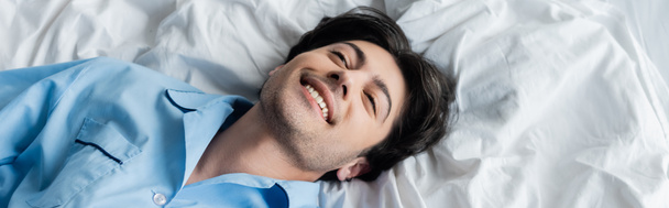 Draufsicht des jungen brünetten Mannes lächelnd auf weißem Bettzeug liegend, Banner - Foto, Bild
