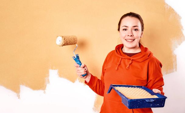 Sorridente donna caucasica pittura parete interna della casa. Appartamento di ristrutturazione. concetto di riparazione e ridecorazione. copia spazio - Foto, immagini