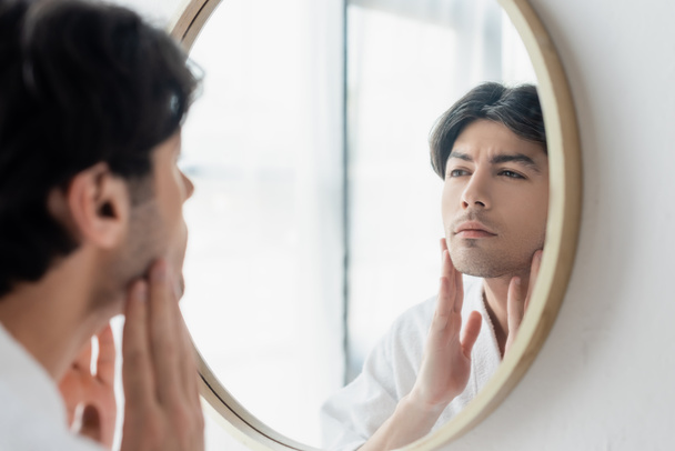 brunette man touching face while looking in bathroom mirror - Φωτογραφία, εικόνα