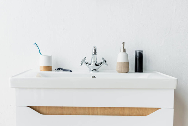 white sink with faucet, dispenser with liquid soap, shaving foam, safety razor and toothbrush - Photo, Image
