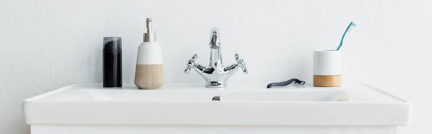 cepillo de dientes, afeitadora de seguridad, jabón líquido y espuma de afeitar en fregadero blanco con grifo, pancarta - Foto, imagen