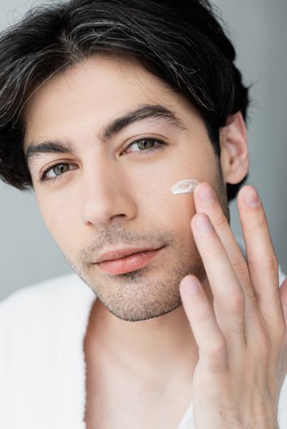close up view of young man applying face cream and looking at camera - Foto, Bild