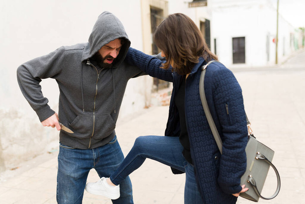 ¡Déjame en paz! Mujer joven pateando y defendiéndose de un atacante armado después de intentar ser robada en la calle - Foto, imagen