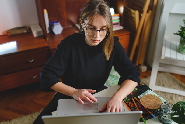 Одна молодая кавказская студентка, работающая за своим ноутбуком, сидя за столом дома, пишет на машинке онлайн-обучение и концепцию образования, проверяя результаты тестов или интернет-покупки. - Фото, изображение