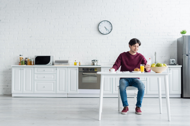 full length άποψη του ανθρώπου κοιτάζοντας smartphone, ενώ έχοντας πρωινό στην ευρύχωρη κουζίνα - Φωτογραφία, εικόνα