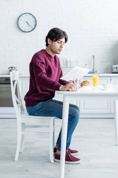 pełny widok długości człowieka czytanie porannej gazety w pobliżu śniadania na stole kuchennym - Zdjęcie, obraz