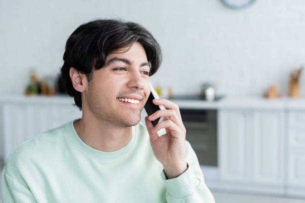 happy young man talking on smartphone in blurred kitchen - Фото, зображення