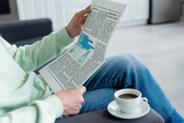 recortado vista del hombre leyendo periódico cerca de taza de café en el sofá - Foto, imagen