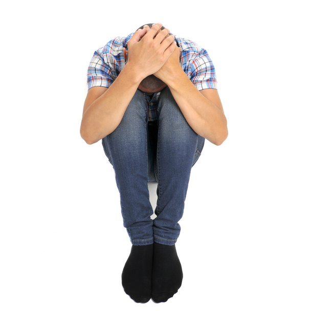 mladý muž stočený v podlaze s hlavou mezi koleny - Fotografie, Obrázek