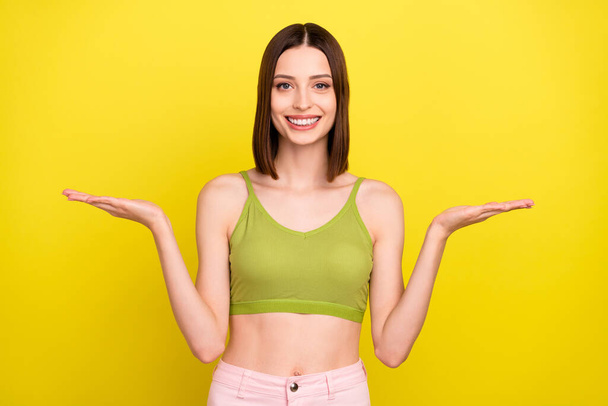 Photo of optimistic brunette young lady hold promo wear green top jeans isolated on yellow color background - Photo, image