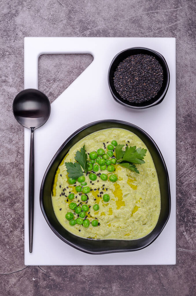 Зелений вершковий суп з горохом і насінням кунжуту в керамічній мисці на фоні шиферу. Вибірковий фокус. Вид зверху
. - Фото, зображення