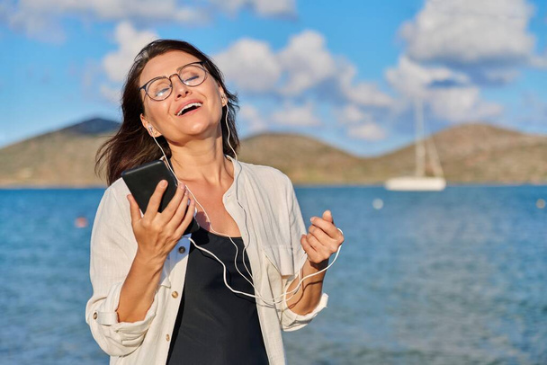 Happy woman in headphones listening to music using smartphone on beach - Foto, Bild