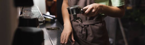 Обрезанный вид на бариста, держащего портативный фильтр возле кофеварки в кафе, баннер  - Фото, изображение